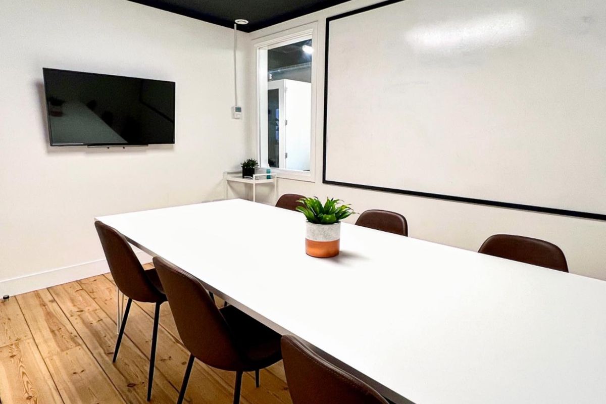 A modern office meeting room featuring hardwood flooring, a large wall-mounted whiteboard, and a clean, minimalist aesthetic suitable for professional collaboration.