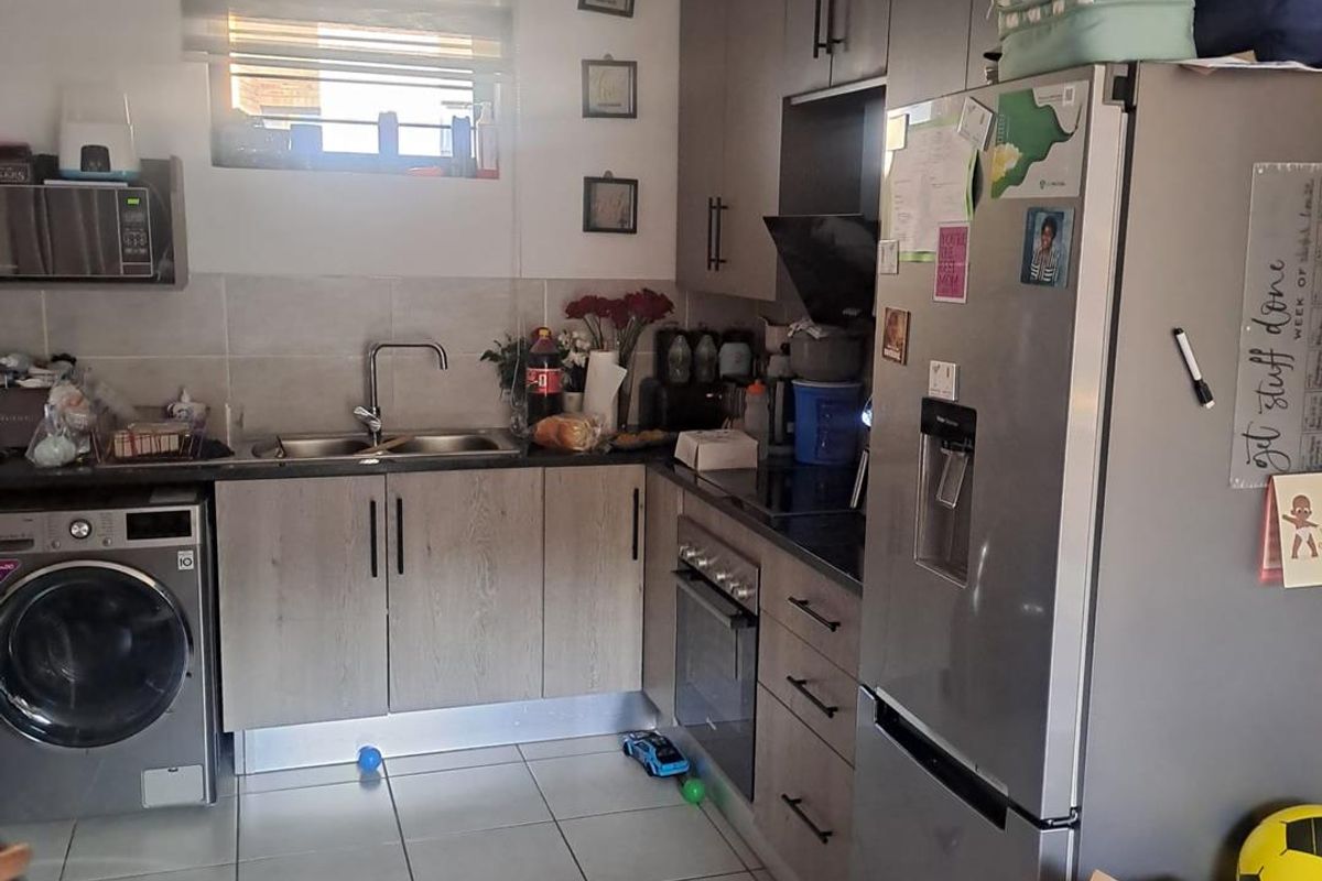 A functional kitchen featuring modern wood-look cabinetry, integrated appliances, tiled flooring, and a tiled backsplash, providing a practical workspace for daily cooking.