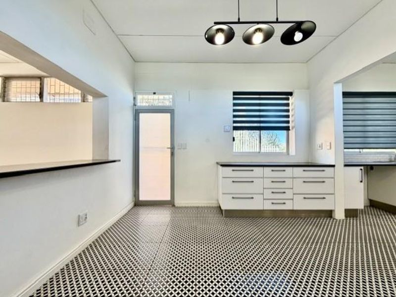 A bright, modern kitchen featuring clean white cabinetry, patterned tiled flooring, and a convenient pass-through window connecting to the adjacent living space.