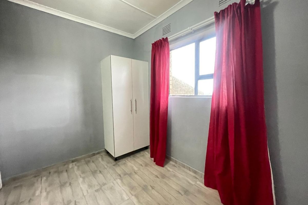 A simple, vacant bedroom featuring light-toned tiled flooring, grey walls, and a built-in wardrobe.