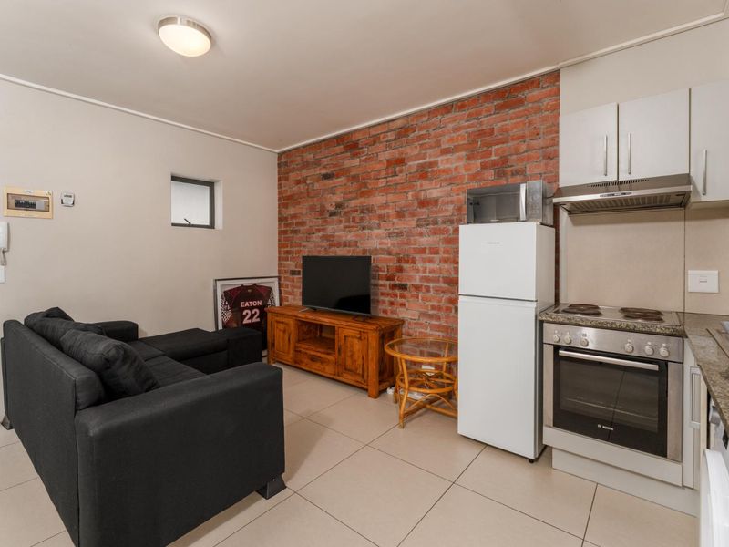 Open-plan living area featuring an exposed brick wall, tiled flooring, and a compact kitchen equipped with a built-in oven, cooktop, and extractor fan.