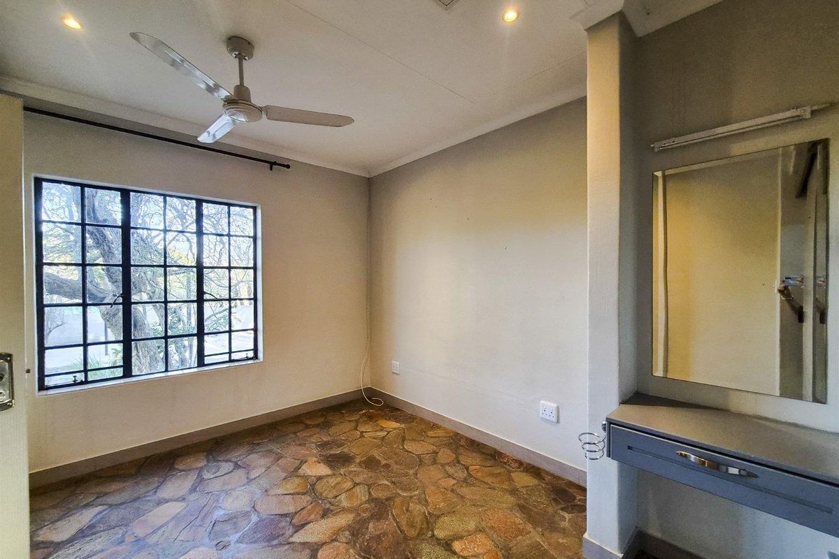 An empty bedroom featuring unique stone flooring, a built-in vanity with mirror, ceiling fan, and large grid-pattern windows providing natural light.