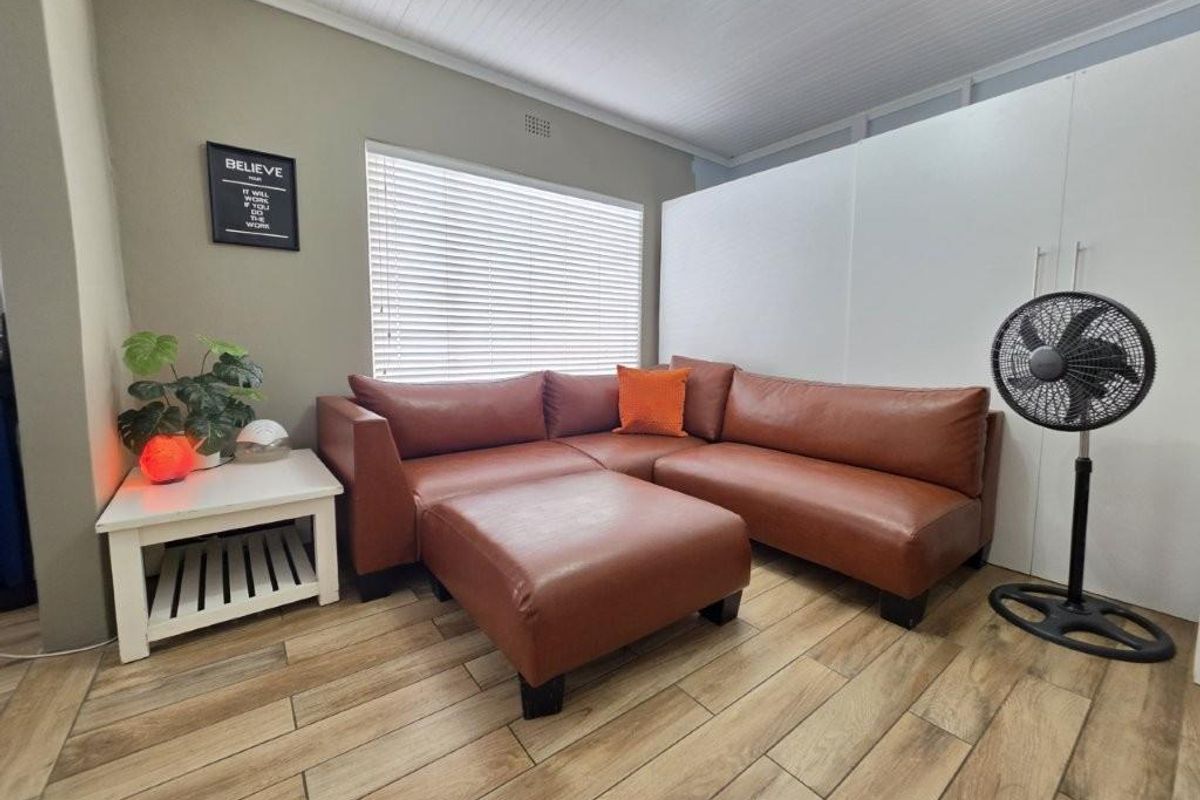 A comfortable living room featuring wood-look tile flooring, a tongue and groove ceiling, and large windows fitted with venetian blinds.