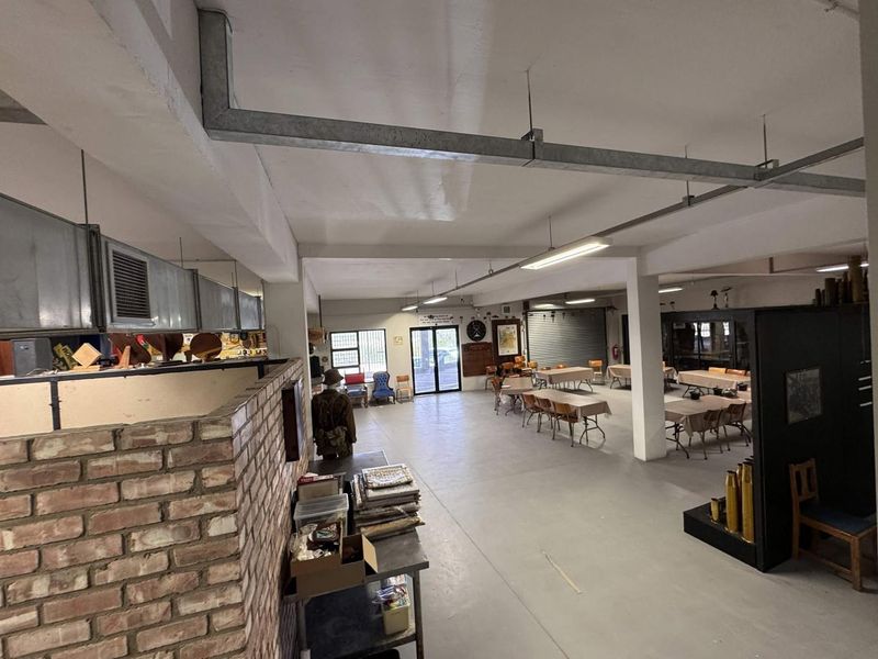 A large, open-plan clubhouse or utility space featuring exposed industrial ductwork, concrete flooring, and a brick partition wall, suitable for versatile commercial or community use.