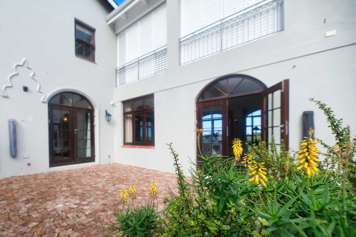 A well-maintained rear courtyard featuring brick paving, arched timber doors, and a balcony with metal railings, providing a seamless indoor-outdoor flow.