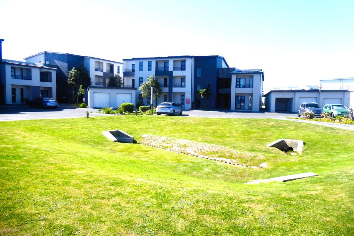 Exterior view of a modern apartment complex featuring paved driveways, garage units, and a well-maintained communal lawn area with integrated drainage.