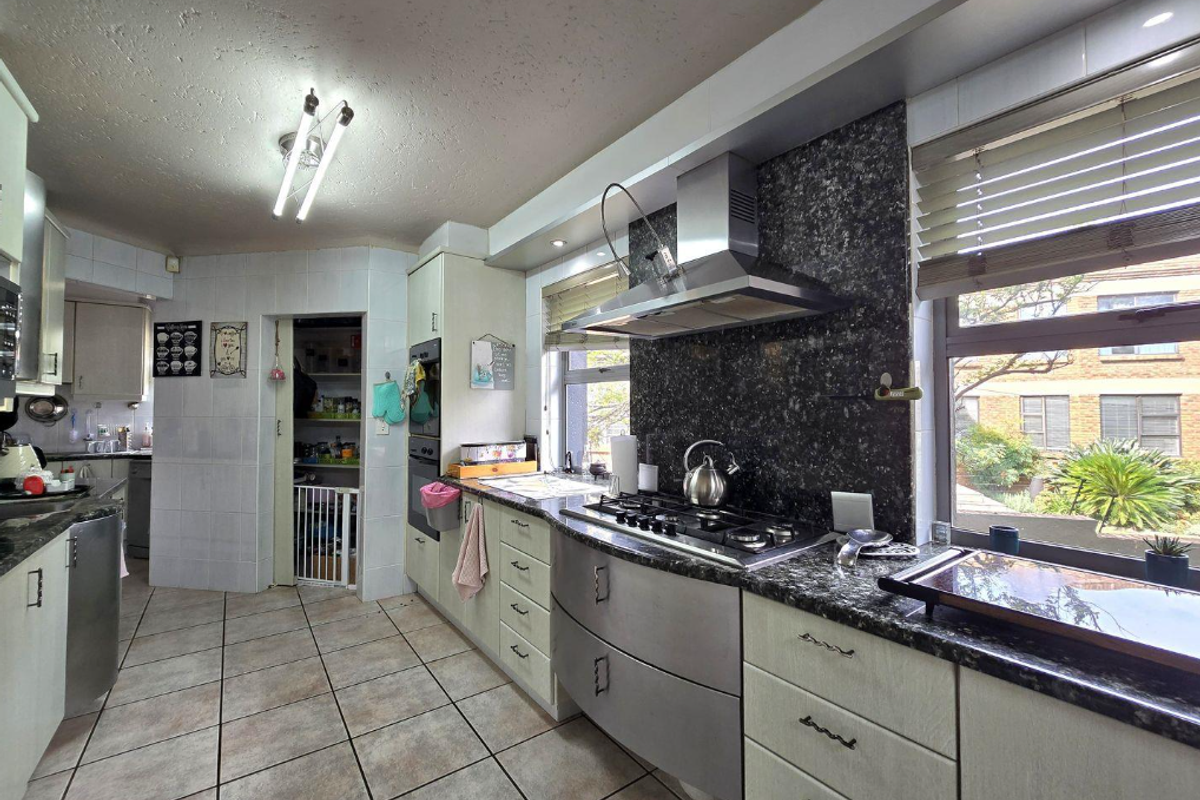 A functional kitchen featuring granite countertops, a gas hob with stainless steel extractor, built-in oven, and an adjacent scullery area.