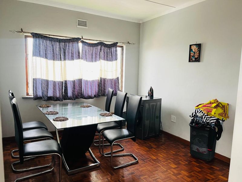 A dining room featuring classic parquet flooring and a large window, providing a functional space for family meals.