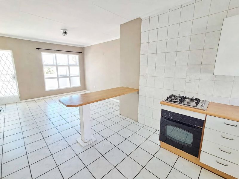 Open-plan kitchen and living area featuring tiled flooring, a built-in oven with gas hob, and a breakfast bar counter.