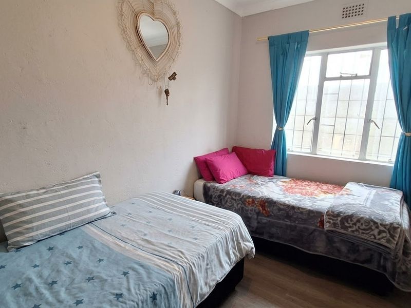 A bedroom featuring laminate flooring, a window with security bars, and a ceiling vent. The walls show signs of wear and cracking.