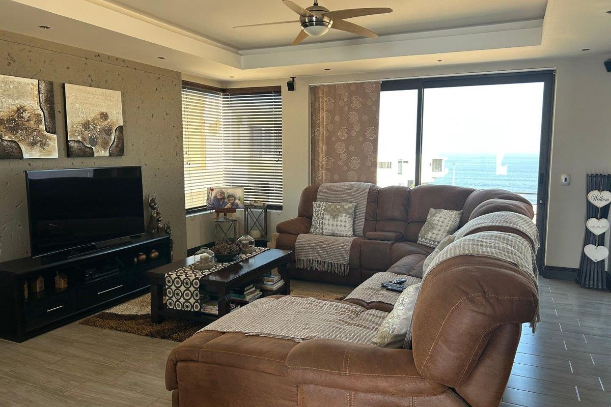 Spacious living room featuring a modern feature wall, ceiling fan, and large sliding glass doors that offer expansive ocean views.