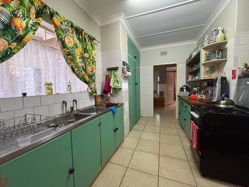 A functional kitchen featuring dated green cabinetry, a double basin sink, tiled splashbacks, and ceramic floor tiles, offering potential for modern renovation.