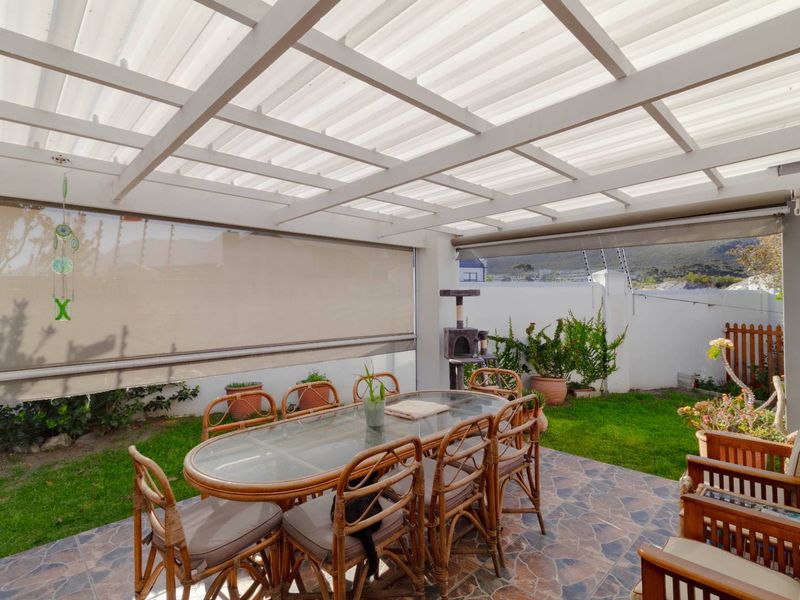 A covered outdoor patio featuring a translucent roof, tiled flooring, and retractable blinds, overlooking a private garden area with boundary wall and electric fencing.