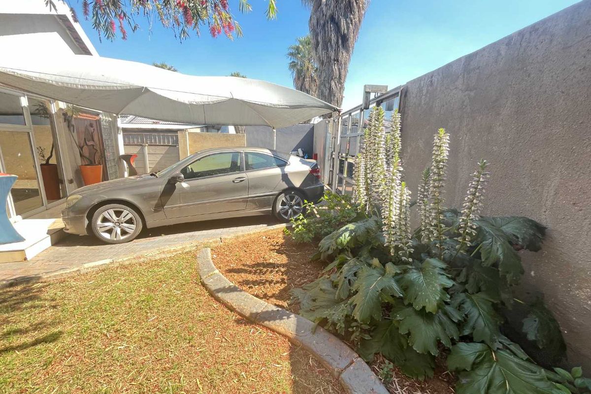 Rear exterior area featuring a paved driveway with a shade sail structure, adjacent to a garden bed and boundary wall.