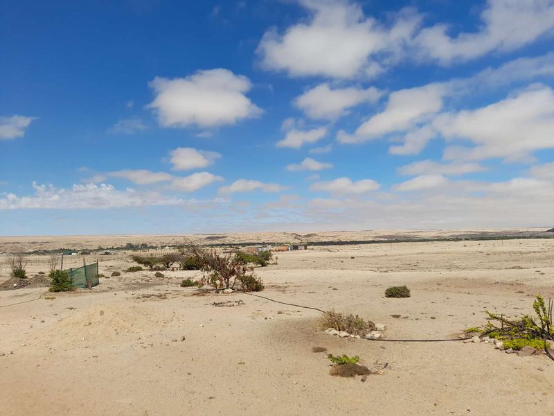 A wide-angle view of the expansive, arid landscape surrounding the small holding, featuring natural terrain and basic perimeter fencing.