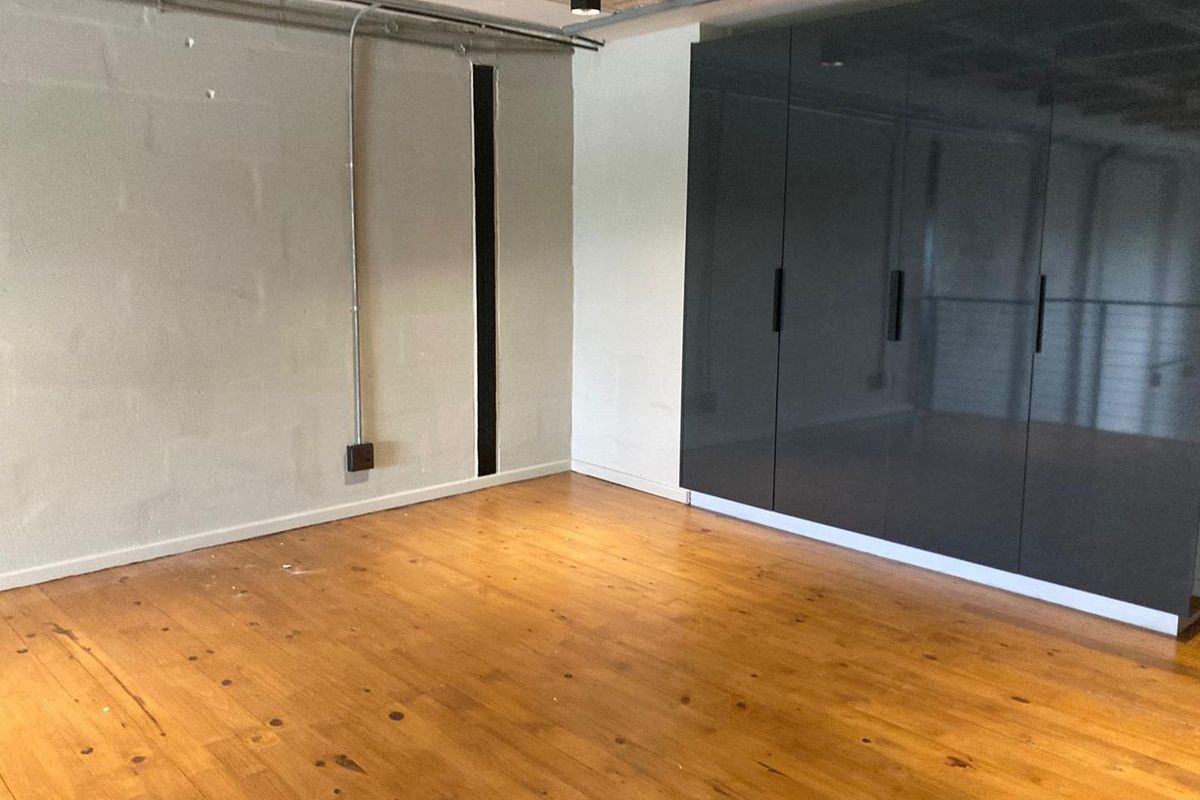 A spacious bedroom featuring polished wooden flooring, built-in dark grey cabinetry, and an industrial-style exposed ceiling and conduit design.