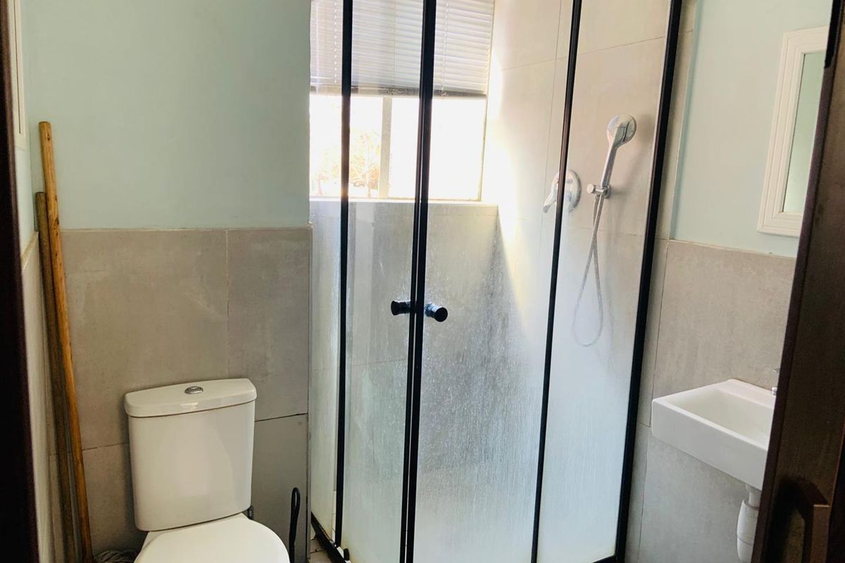 Compact bathroom featuring a modern black-framed shower enclosure, wall-mounted basin, and standard toilet with neutral wall tiling.