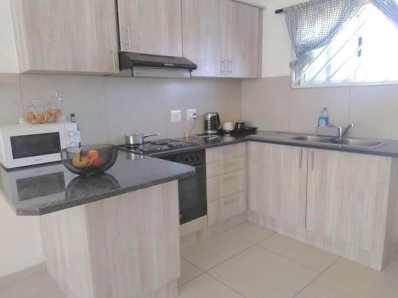 A functional kitchen featuring light wood-finish cabinetry, granite countertops, a built-in oven with gas hob, and tiled flooring.