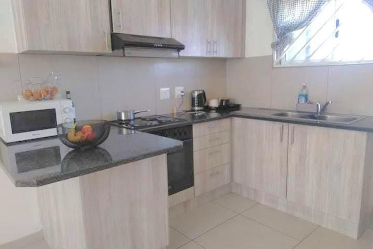 A functional kitchen featuring light wood-finish cabinetry, granite countertops, a built-in oven with gas hob, and tiled flooring.
