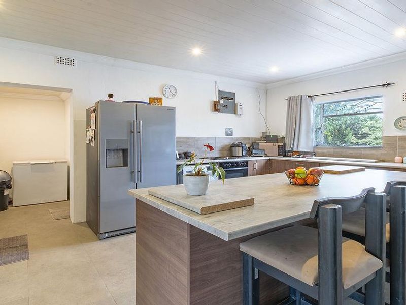 A functional kitchen featuring a central island, ample cabinetry, tiled splashbacks, and an adjoining scullery area with neutral floor tiles and recessed lighting.