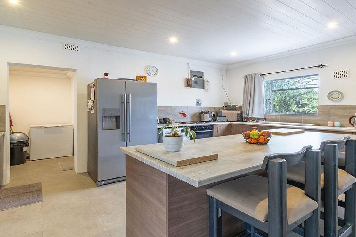 A functional kitchen featuring a central island, ample cabinetry, tiled splashbacks, and an adjoining scullery area with neutral floor tiles and recessed lighting.