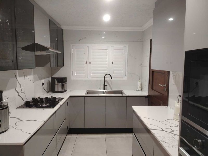 Modern kitchen featuring high-gloss cabinetry, marble-look quartz countertops, gas hob, built-in oven, and plantation shutters.