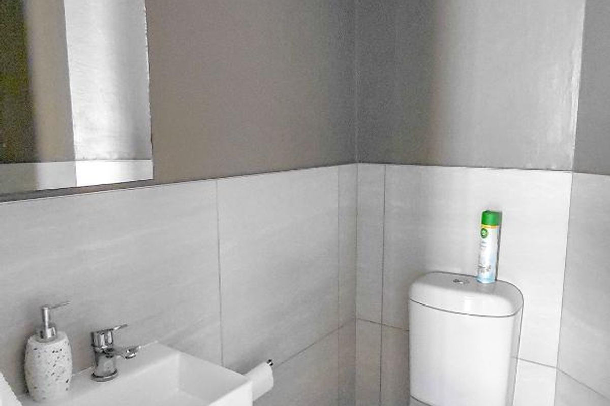 A compact, modern guest bathroom featuring a wall-mounted basin, a standard toilet, and neutral tiled walls.