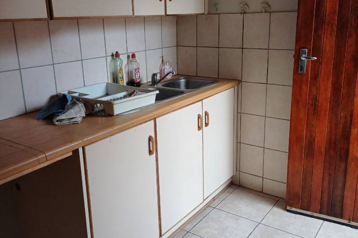 A functional scullery area featuring built-in cabinetry, a stainless steel sink, and tiled flooring, providing practical utility space for the home.