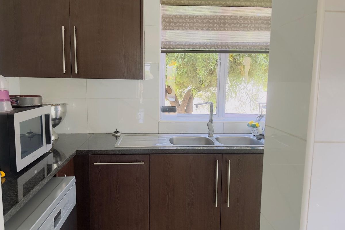 A functional kitchen area featuring dark wood cabinetry, granite countertops, a double stainless steel sink, and tiled splashbacks.