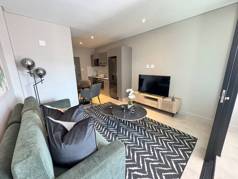 Modern open-plan living area featuring a compact kitchen with built-in cabinetry and integrated appliances, seamlessly flowing into the lounge space.