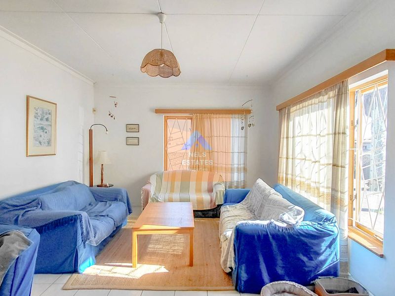 A bright living room featuring tiled flooring, large windows with security bars, and a central pendant light fixture.