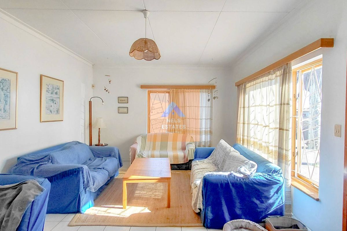 A bright living room featuring tiled flooring, large windows with security bars, and a central pendant light fixture.
