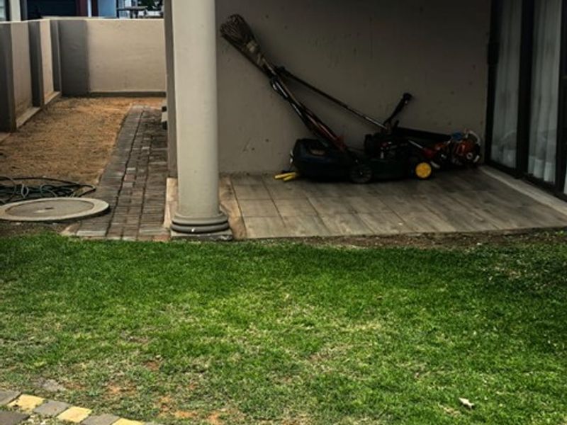 A covered patio area featuring tiled flooring and a decorative column, overlooking a garden with a paved walkway and boundary wall.