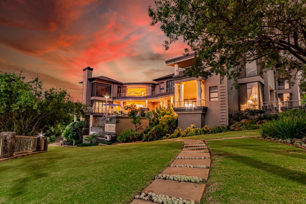 A stunning multi-level luxury residence featuring expansive terraces, large glass windows, and beautifully landscaped gardens at sunset.