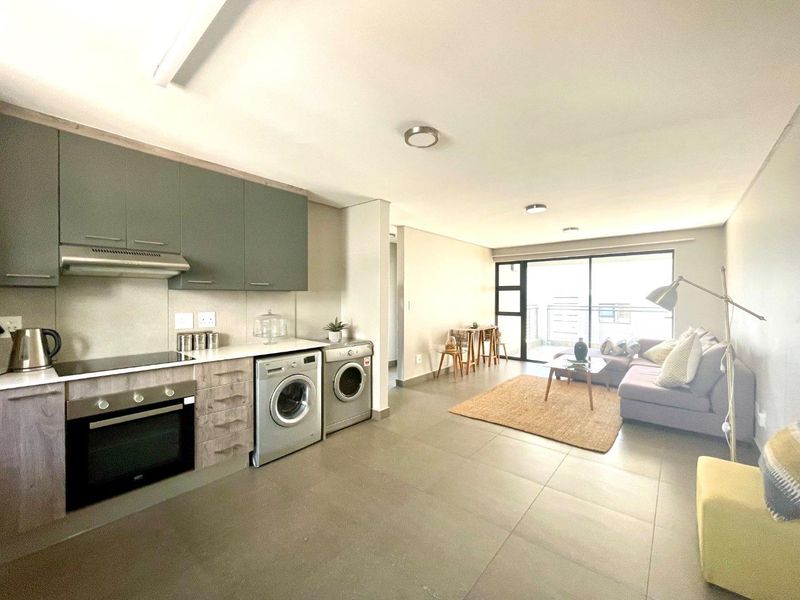 Modern open-plan living area featuring a contemporary kitchen with built-in appliances, tiled flooring, and seamless access to a balcony through large sliding glass doors.