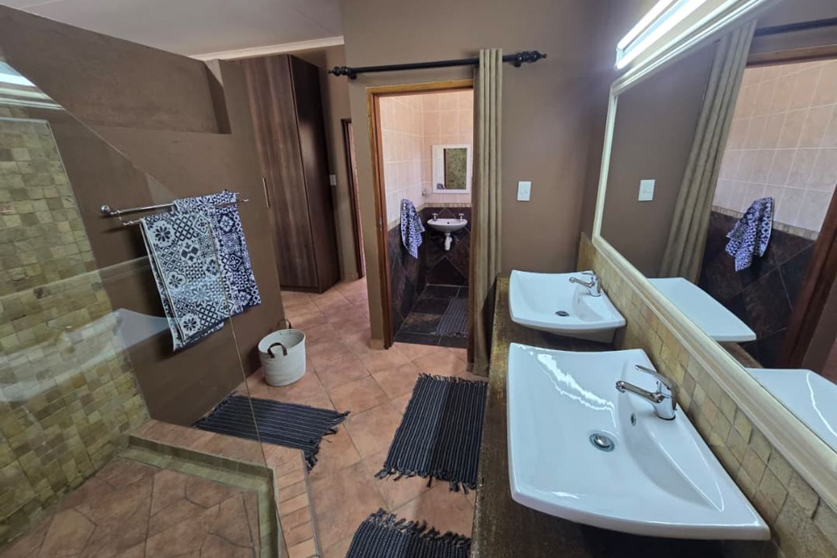 Spacious bathroom featuring a double vanity with integrated sinks, a walk-in shower with mosaic tiling, and a separate toilet area.