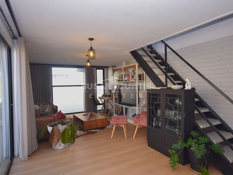 Open-plan living area featuring timber flooring, an exposed brick feature wall, and a modern staircase leading to the upper level.
