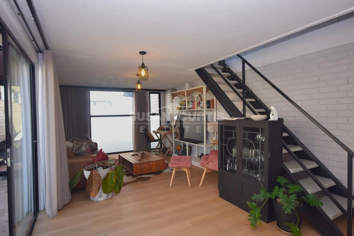 Open-plan living area featuring timber flooring, an exposed brick feature wall, and a modern staircase leading to the upper level.