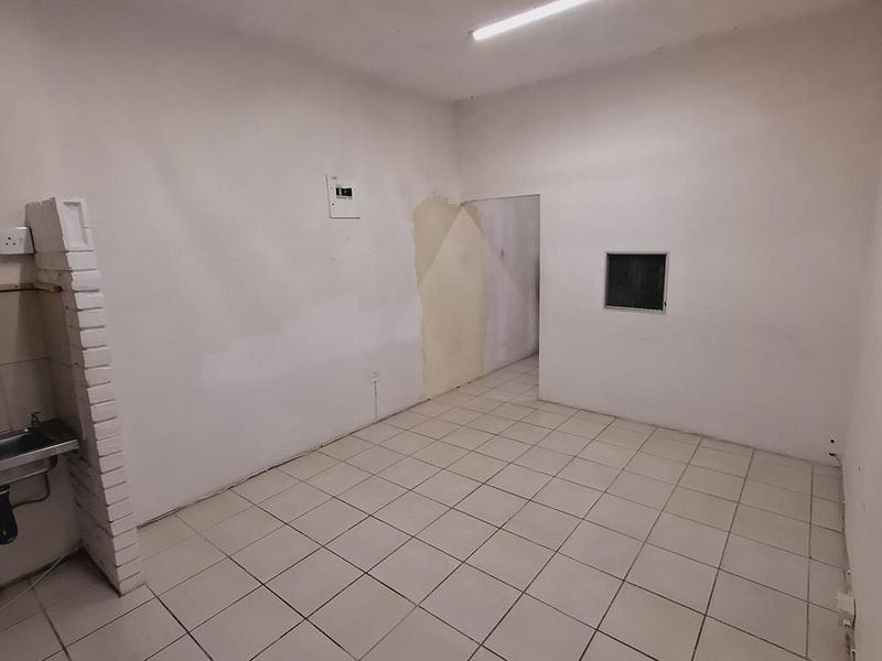 An empty office space featuring tiled flooring, a small sink area with brick detailing, and visible wall surface imperfections requiring maintenance.