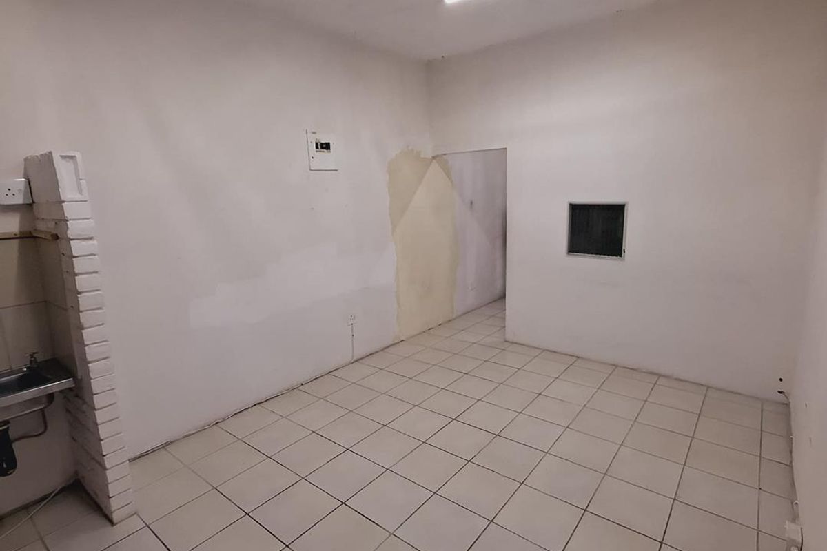 An empty office space featuring tiled flooring, a small sink area with brick detailing, and visible wall surface imperfections requiring maintenance.