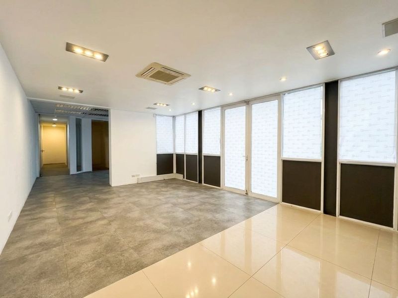 A bright, modern, and empty office space featuring large glass windows, recessed ceiling lighting, ducted air conditioning, and contemporary tiled flooring.