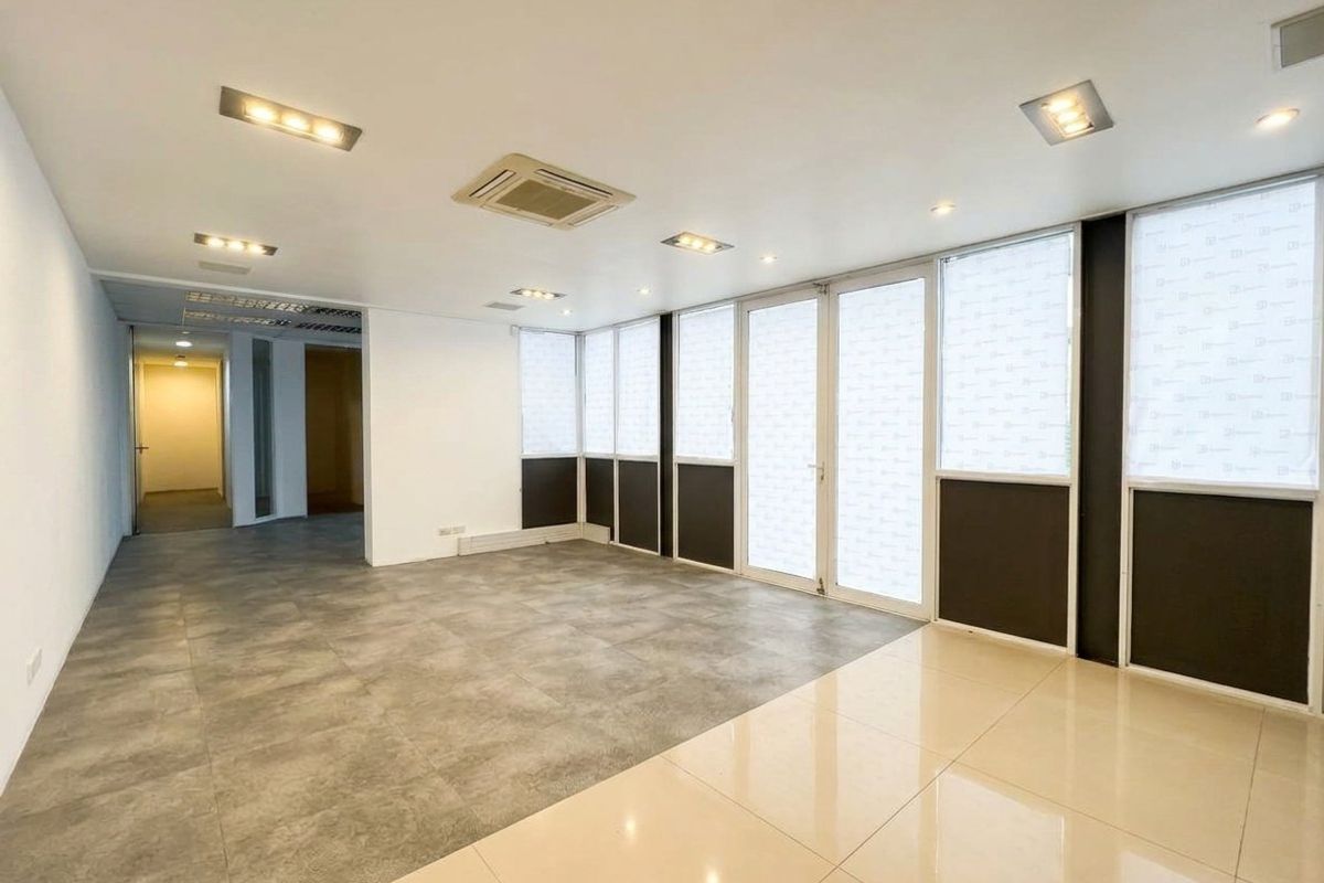 A bright, modern, and empty office space featuring large glass windows, recessed ceiling lighting, ducted air conditioning, and contemporary tiled flooring.