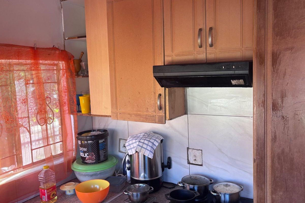 A compact kitchen area featuring wooden cabinetry, a built-in extractor fan, and tiled splashbacks, offering a functional space for meal preparation.