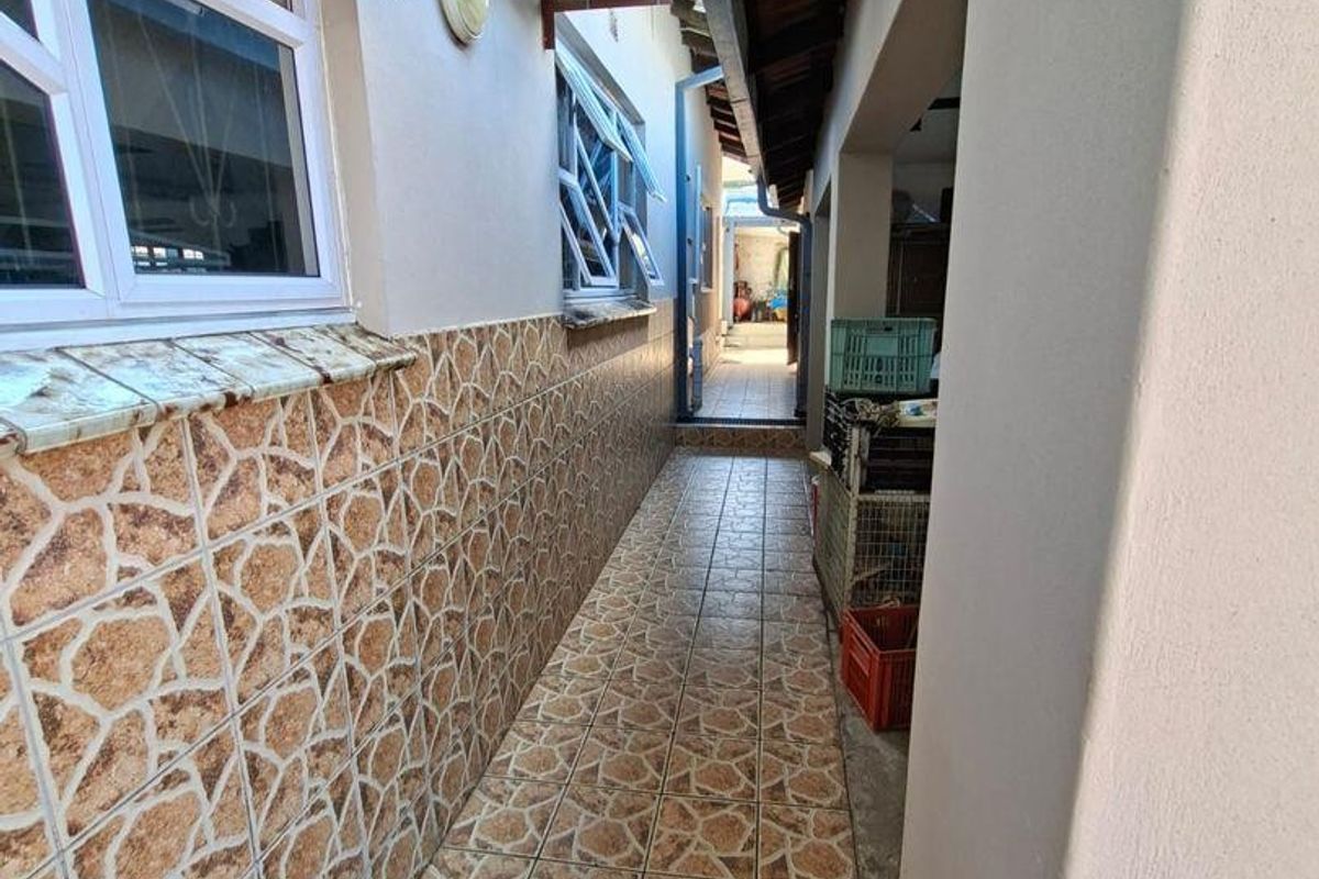 A narrow exterior side passage featuring tiled flooring and wall cladding, with mounted air conditioning unit and security windows.