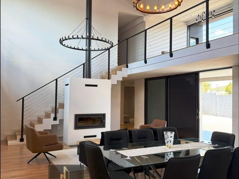 Spacious open-plan living and dining area featuring a double-volume ceiling, a central built-in fireplace, a mezzanine level, and large sliding doors to the exterior.