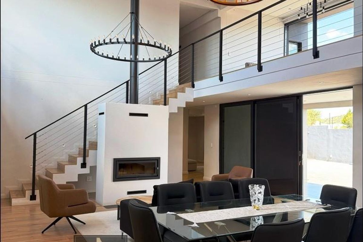 Spacious open-plan living and dining area featuring a double-volume ceiling, a central built-in fireplace, a mezzanine level, and large sliding doors to the exterior.