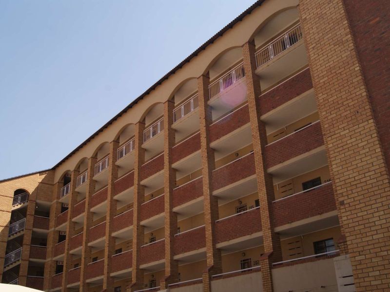 A multi-story apartment building exterior featuring face brick construction, arched balcony openings, and metal railings.