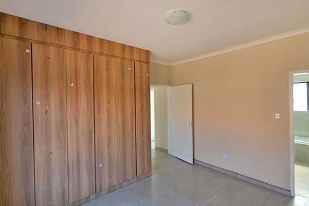A bright bedroom featuring built-in wooden cupboards, tiled flooring, and direct access to an adjoining bathroom.