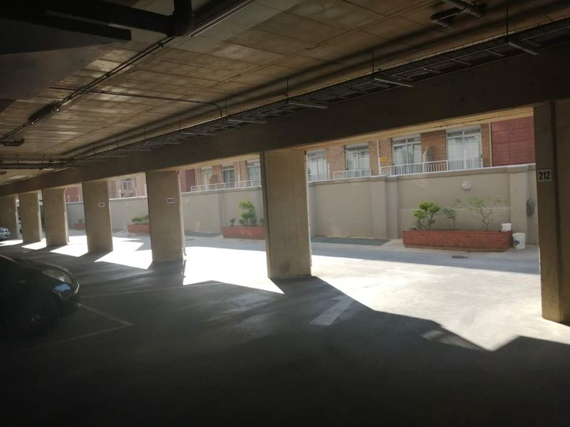 A covered parking garage area featuring concrete structural columns, overhead cable management, and exterior brick planter boxes.