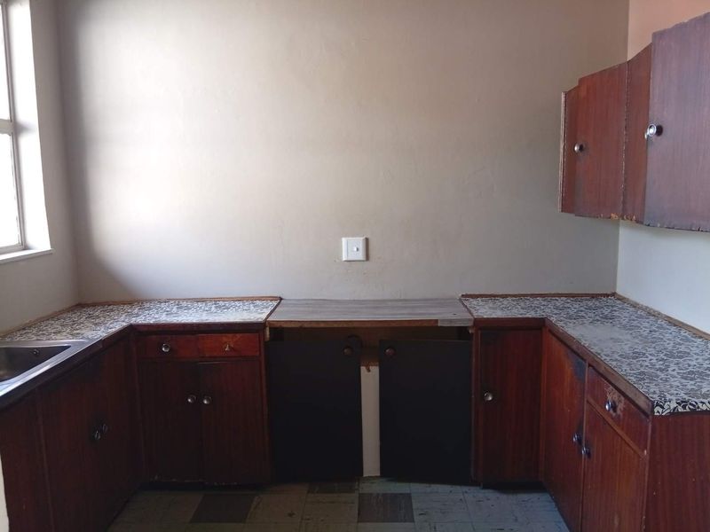 A dated kitchen featuring original wooden cabinetry, laminate countertops, and a stainless steel sink, offering a blank canvas for a modern renovation.